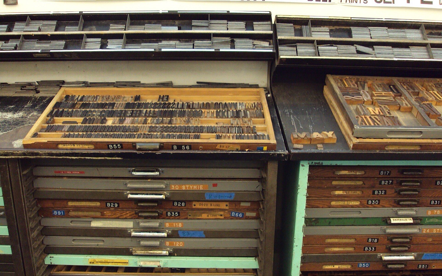 Banks of wooden type cabinets beneath a wall of specimen posters